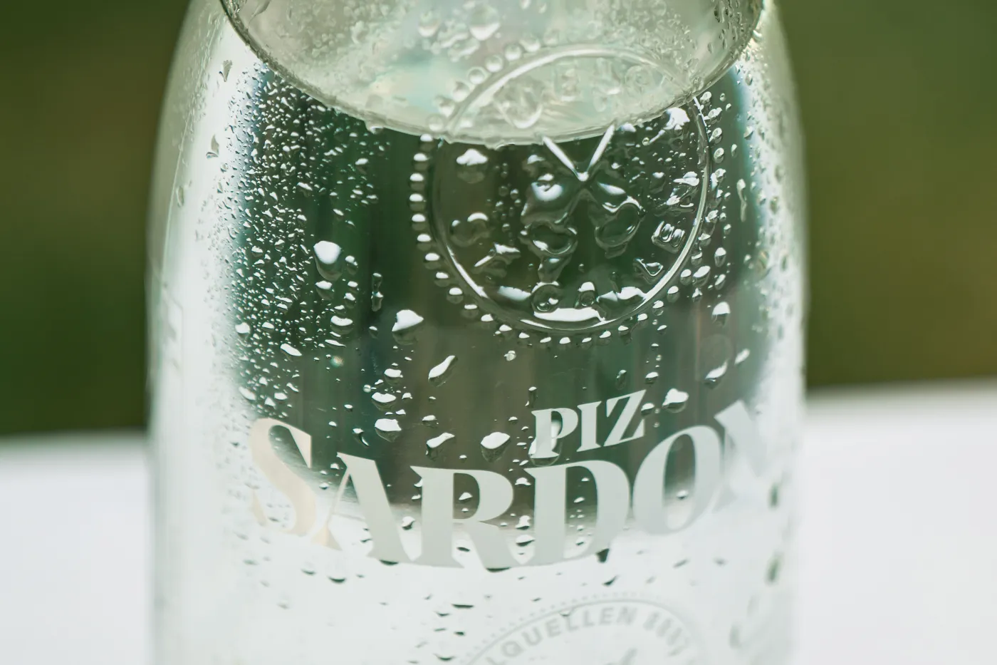 Nahaufnahme einer beschlagenen Piz-Sardona-Glasflasche mit Wassertropfen, Wappen und Schriftzug